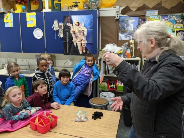 Hilary Hart shows students at Roosevelt Elementary school trout eggs that are about to be dropped into the tank